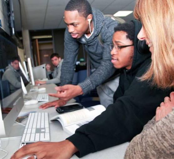 two men and professor look at computer in the mac lab